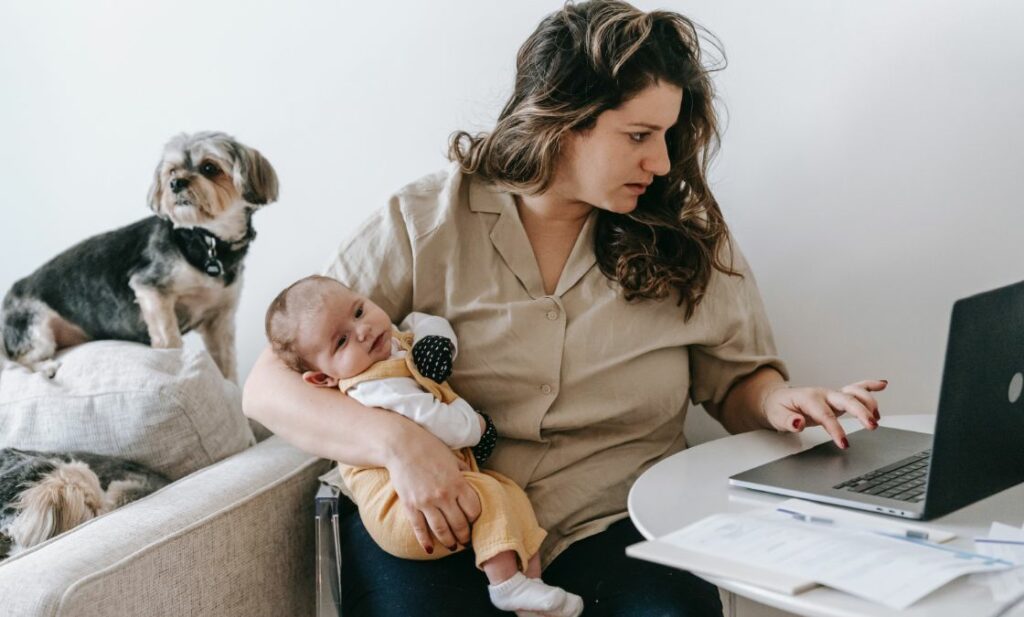 Woman holding baby working on laptop
